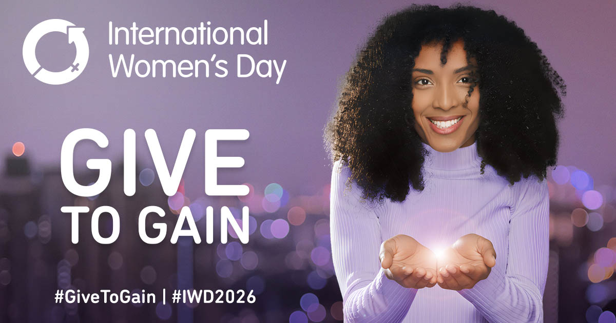 This image is a promotional graphic for International Women's Day 2026, featuring a purple and lilac color scheme with a city bokeh background. Here are the key elements: Central Figure: A smiling woman wearing a lilac turtleneck holds her hands out, cupping a glowing light as if she is offering or receiving something precious.