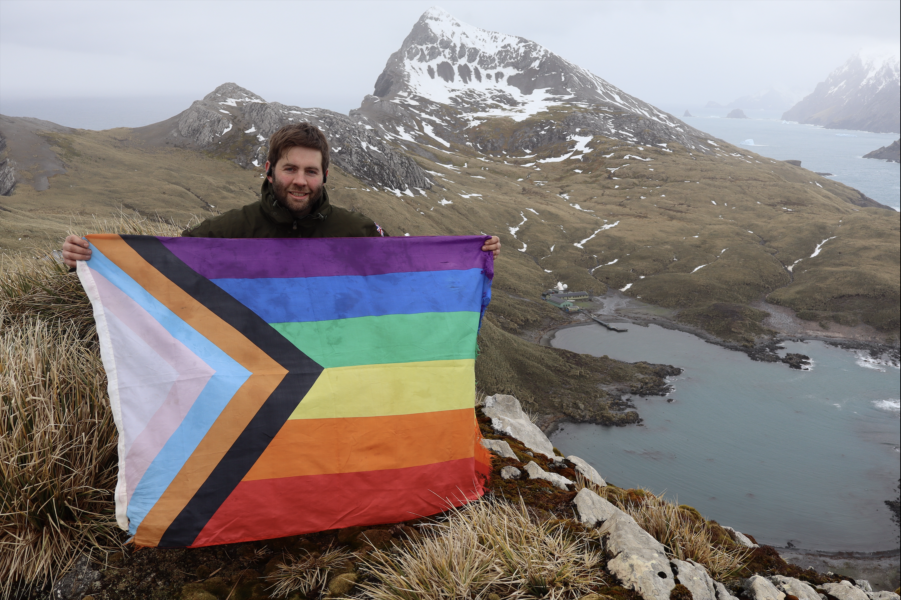 Adam Owen proudly displays the Polar Pride flag with the station in the background.