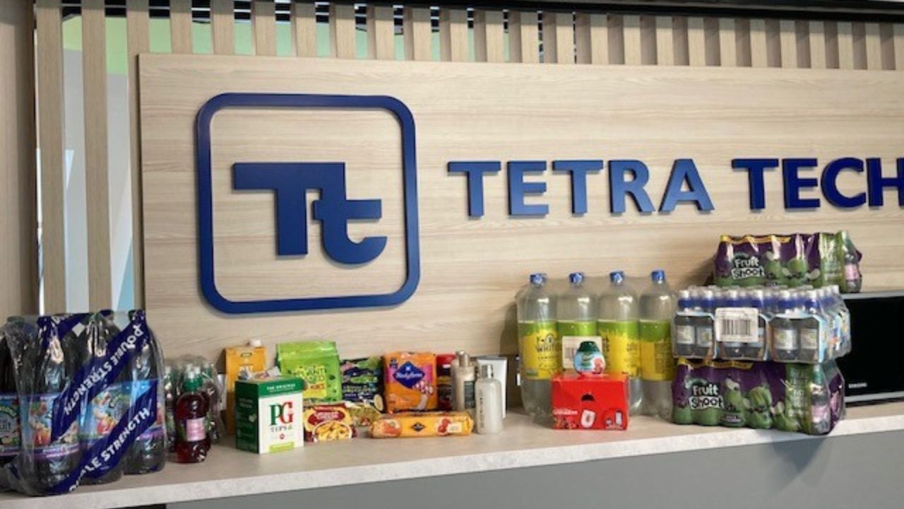 This image features a collection of donated goods neatly arranged on a counter in front of a Tetra Tech corporate sign. The items include various household essentials