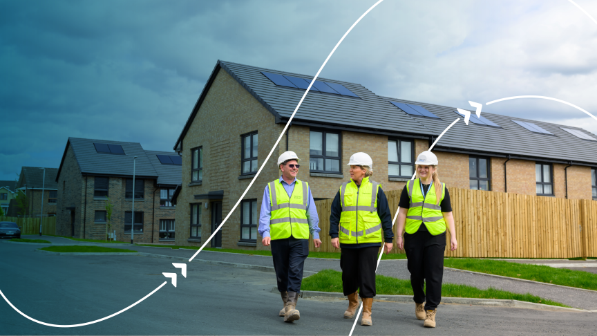 The People Three Workers: There is one man on the left and two women in the middle and on the right, all walking side by side towards the camera.  Safety Gear: Every individual is wearing high-visibility neon green/yellow vests, white hard hats, and work boots. The man is also wearing sunglasses.  Interaction: They appear engaged in casual conversation, smiling and looking towards each other as they walk.  The Setting Housing Development: They are walking on an asphalt road in front of modern, two-storey brick houses. The houses have dark grey tiled roofs equipped with solar panels. Wooden fencing lines the properties.  Split Overlay Graphic: The image is divided diagonally by a dynamic graphic element.  The left side is filtered with a dark blue overlay, casting a stormy or shadowed mood over the background houses.  The right side transitions into bright, natural daylight with a clearer sky, suggesting a theme of progress, transition, or moving towards a brighter, sustainable future.  White Graphic Curves: Curved white lines with arrowheads sweep across the image, reinforcing a concept of motion, energy flow, or forward planning.