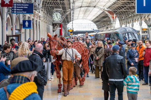 The horse puppet being led through the train station