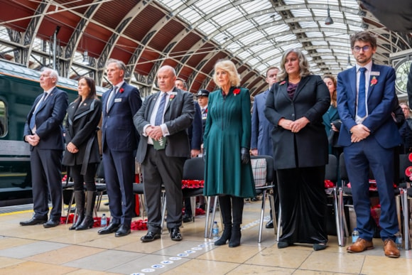 The Queen standing with a group of mixed gender people in a train station
