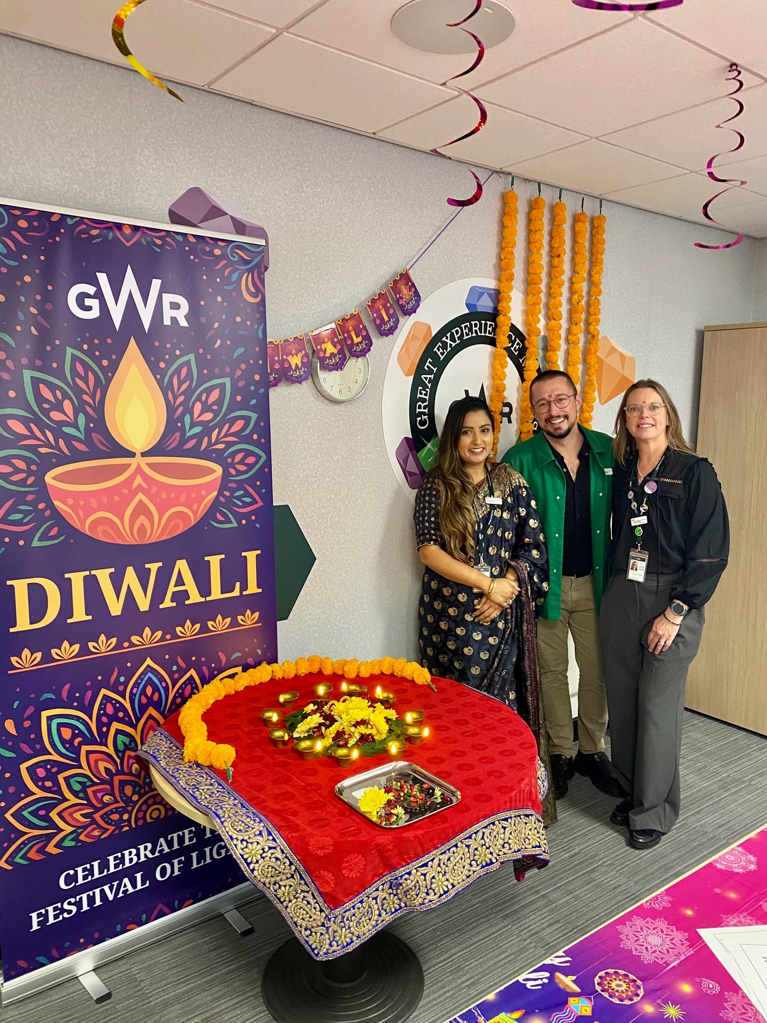 a group of diverse gender and ethnicities standing in front of a GWR Diwali poster