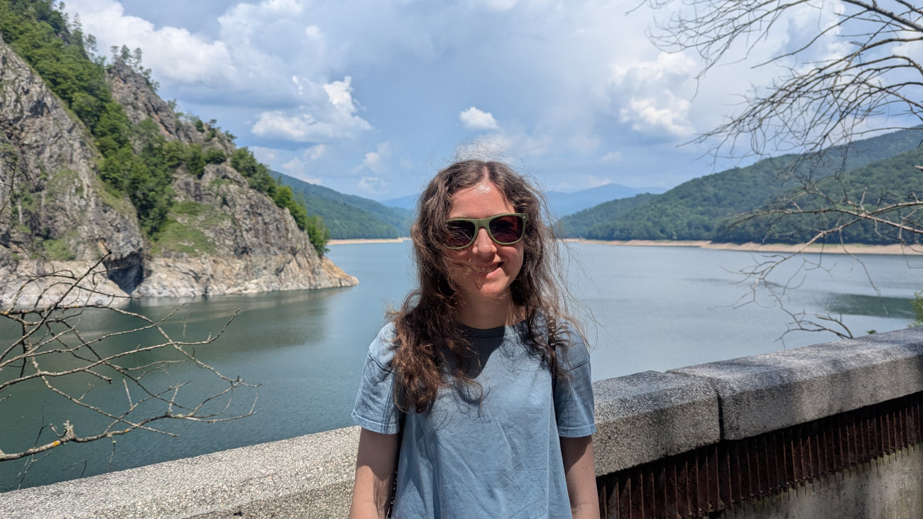 Rachel standing in front of a lake with trees and hills on either side