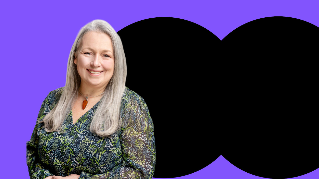Joanne with blond hair in front of a purple and black banner