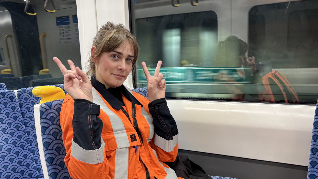 Zoe sitting on a train is a orange hi ves jacker