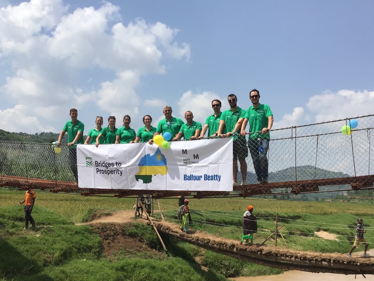 Mott MacDonal collegues standing on a bridge in Kenya, wearing green thirts and holding a banner