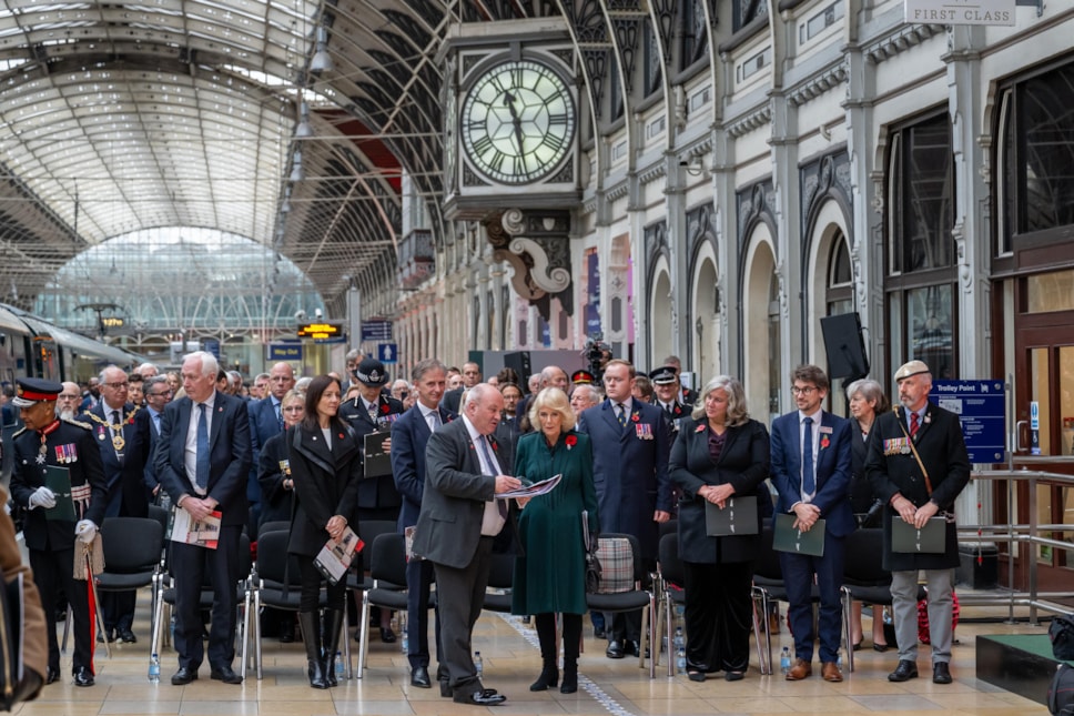A group of diverse gender and races standing in a group with the Queen in a railway station