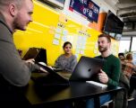 3 people sat around a table with laptops working