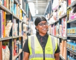 A african women smiling in a warehouse setting wearing a yellow hi-ves vest