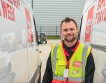 A  Sainsbury's driver, a white male, stands between two delivery vehicles