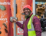 A black male driver for Sainsbury's closes the door to a delivery vehicle