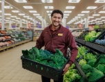 An Asian male employee standing in a Sainsbury shop holding a crate of fresh produce