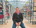 A white male sitting on a stool in a warehouse setting
