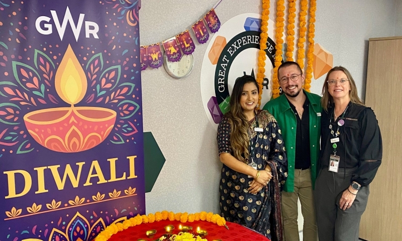 a group of diverse gender and ethnicities standing in front of a GWR Diwali poster