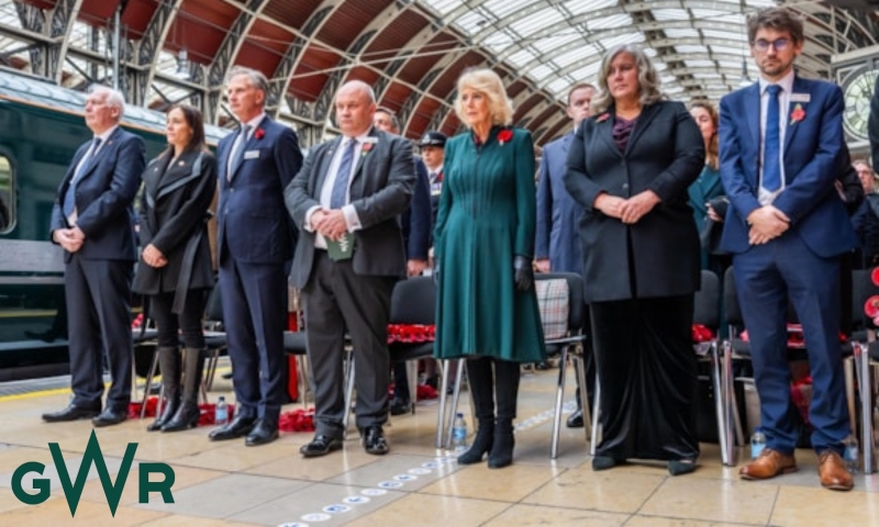 A group of diverse gender and races standing in a group with the Queen in a railway station