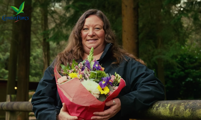 The image features a woman smiling warmly at the camera while holding a large, colorful bouquet of flowers.