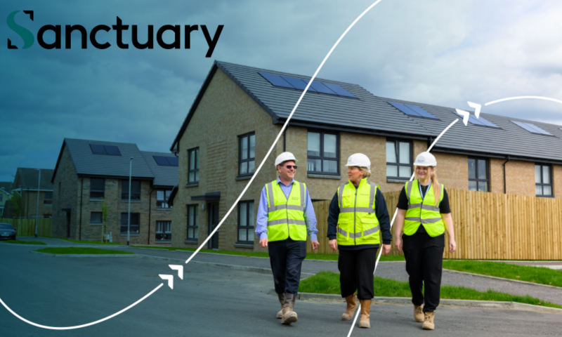 This image features three construction or housing professionals walking through a newly built residential housing development in the UK.  Here is a breakdown of the key elements in the image:  The People The Group: There are three individuals—one man on the left and two women to his right—walking side-by-side along a paved road or pathway. They appear to be smiling and engaged in conversation.  Attire: All three are wearing professional site safety gear, including white hard hats, high-visibility yellow/green reflective vests, dark trousers, and sturdy work boots.  The Setting The Houses: The background showcases modern, two-story residential homes built with light-coloured brick or stone. The roofs are fitted with dark grey tiles and feature solar panels, highlighting a focus on energy efficiency or sustainability.  Surroundings: The houses have neatly fenced backyards, paved driveways, and small patches of green grass along the kerbs. The sky is somewhat overcast with white and grey clouds.  Graphic Overlay & Branding Branding: In the top left corner, the word "Sanctuary" is prominently displayed in a clean, black sans-serif font, with a stylised green 'S' logo. (This refers to Sanctuary, a major housing and care provider in the UK).  Design Elements: A dark blue-teal gradient overlay fades in from the left side of the image. Sweeping white curved lines with arrowheads cut across the graphic, giving the image a dynamic, forward-moving corporate look.