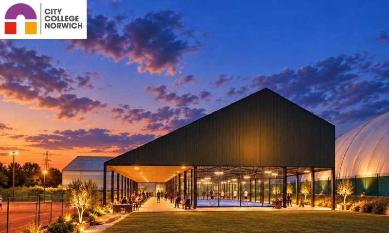 A modern sports pavilion stands beneath a dramatic dusk sky streaked with vibrant orange, pink, and deep indigo clouds.   The centrepiece is an asymmetrical, dark-clad pavilion featuring a pitched roof supported by black structural pillars. Beneath its shelter, brightly lit padel courts with blue playing surfaces are enclosed in glass, with players in mid-game. Running parallel to the courts is an open-sided, covered walkway with warm downlighting embedded in the ceiling, where people are socialising and seated at café-style tables.   To the left, an outdoor tennis court is enclosed by chain-link fencing, where a figure can be seen playing under the glow of tall floodlights. A gravelled border planted with low shrubbery and small trees in illuminated planters separates the court from a broad, neatly manicured lawn in the foreground.   To the far right, the curved, translucent form of a large air dome is softly illuminated against the nightfall, with an industrial pylon and treeline silhouetted along the distant horizon.